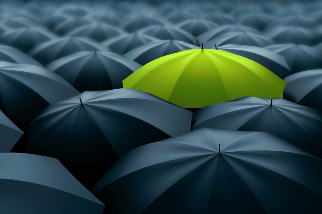 picture showing an umbrellas, one umbrella is green, others are black